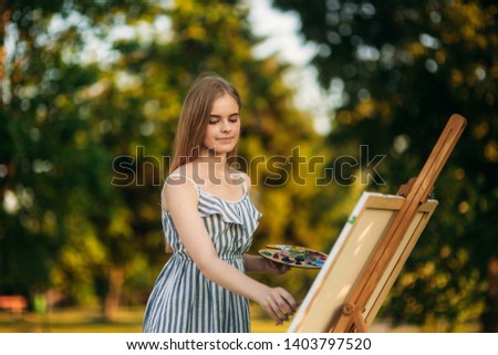 Blond hair girl in dress drawing a picture in the park