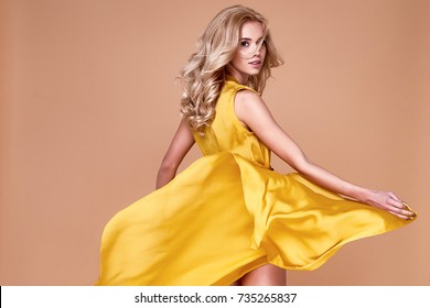 Blond hair woman beautiful face sexy skinny body shape tan skin care wear fashion dress silk yellow color runway model studio catalog clothes style for summer vacation walk date beach party makeup.