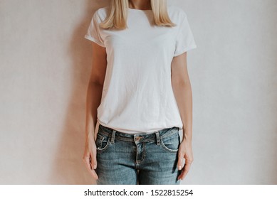 Blond hair woman posing near a light wall. Beautiful young caucasian girl. Hand gestures. Emotion. Casual clothing. Studio model in work. Strong woman, future is female. Jeans and white blank t-shirt