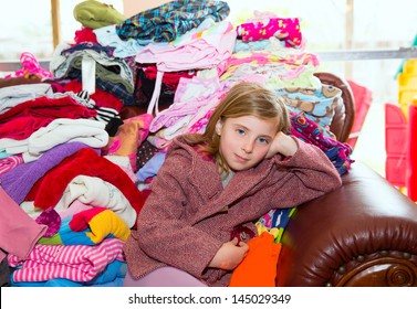 Blond Kid Girl Sitting On A Messy Clothes Sofa Before Folding Laundry