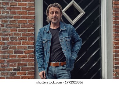 Blond man in jeans with a brown leather belt and a denim jacket in front of front door of an old farmhouse on a sunny day. - Powered by Shutterstock