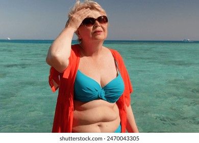 Blond middle aged woman wearing in swimsuit and glasses suffering from abnormal heat near sea beach in sunny summer day, concept, outdoors - Powered by Shutterstock