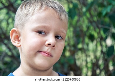 Blond Preschooler Grimaces Making Weird Face Expressions. Boy Has Fun Walking Outdoors In Shade Of Trees In Park On Summer Holiday Closeup