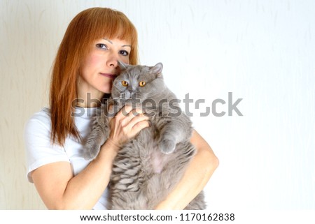 Blond / red hair mature senior female relaxing at home holding and huging cute purring  cat. Attractive middle aged woman with big british shorthair cat resting at home.A woman in period of menopause.