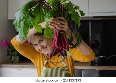 Blond smiling woman holding bunch of beetroots with leaves, cooking fresh organic salad in the kitchen on summer weekend. Eco friendly food, healthy eating and diet at home. Joying farming vegetables