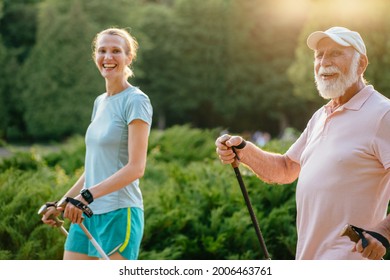 A blond sporty daughter take care of her father 80 year. Senior man very happy when go to walk at summer park, using trekking sticks. Concept care nurse with old people.