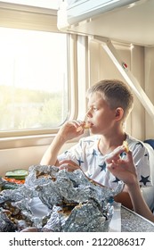 Blond Teen Boy Have Lunch Eating Fried Chicken Sitting At Table In Train Car Against Landscape Outside Window Closeup