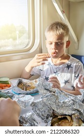 Blond Teen Boy Have Lunch Eating Fried Chicken Sitting At Table In Train Car Against Landscape Outside Window Closeup