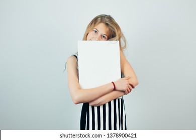 Blond teen girl embracing poster template, grey wall on background. Beautiful girl with blank empty canvas. Copy space for text on canvas board.