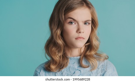 Blond teenage girl raising eyebrow on camera looking serious over blue background. Suspicion expression