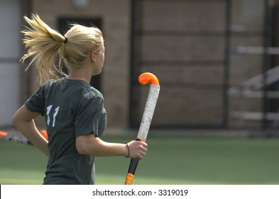 A blond, teenage girl runs across the field holding a bright orange field hockey stick. - Powered by Shutterstock