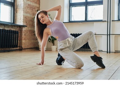 Blond teenage girl in tanktop and sweatpants performing new vogue dance movement on the floor of modern loft studio