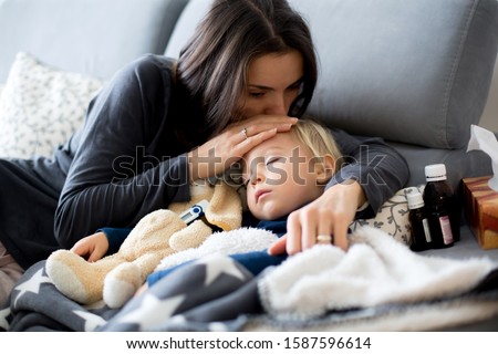 Blond toddler boy, sleeping on the couch in living room, lying down with fever, mom checking on him