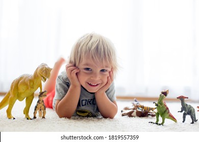 Blondes Kleinkind, spielend mit Dinosauriern zu Hause, schönes, weiches Rücklicht