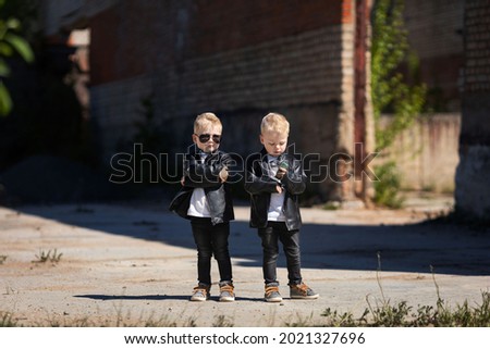 Blond twin boys in dark glasses and leather jackets.The little twins are stylishly dressed in a rock style.Cute kids look like celebrities.A children's photo on the background of an abandoned building
