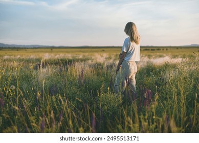 Blond woman back view staying in the floral meadow at sunset - Powered by Shutterstock