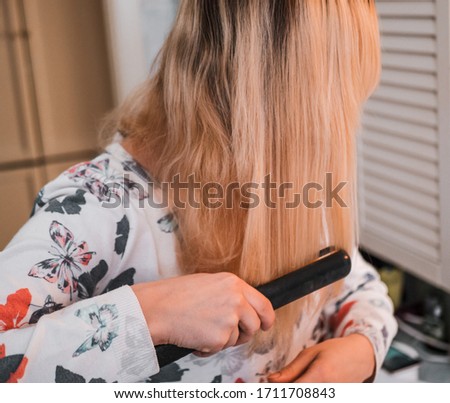 blond woman in the bathroom straightens her hair with a curling iron.