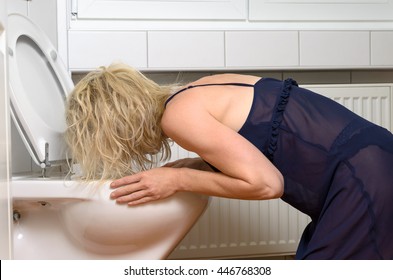 Blond woman in a black dress kneeling down vomiting into a toilet conceptual of an illness or drunkenness after a party