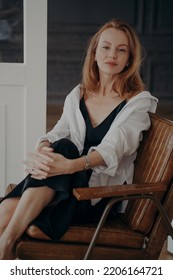 Blond Woman In Black Evening Dress And White Shirt. Stylish Confident Mid Adult Lady Is Sitting In Room. Woman In Luxurious, Vintage, Leather Arm Chair. Happy Caucasian Woman After A Party.