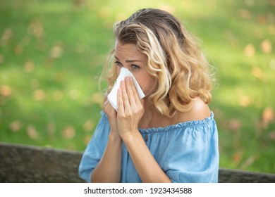 blond woman blowing nose outdoors