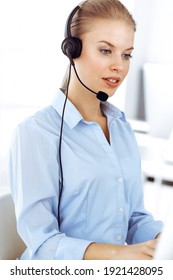 Blond Woman Call Operator Is Using Computer And Headset For Consulting Clients Online. Group Of Diverse People Working As Customer Service Occupation. Business Concept