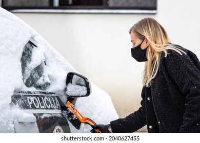 Blond Woman In Face Mask With A Squeegee Cleans Snow From A Police Car