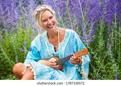 blonde Frau in ihren 40ern, die auf Blumenfeld saß und Gitarre spielte