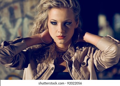 Blond Woman Holding Hands At The Back Wearing Leather Jacket Inside Ruins. Fashion Photo