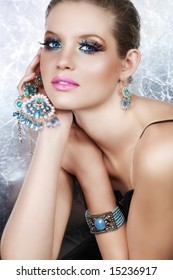 Blond Woman With Long False Lashes Holding Pearl And Blue Stones Golden Jewelry With Dreaming Expression