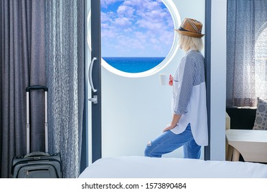 Blond Woman Looking At The View From Hotel Room On Yhe Sea And Blue Sky. Travel, Arrival In Hotel concept. - Shutterstock ID 1573890484