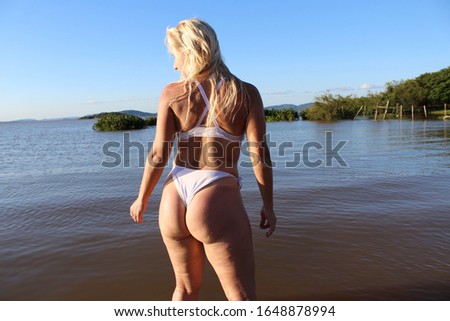Blond woman posing at the beach in he summer on a sunny day with water in the background and blue sky