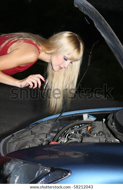 blond woman in\
red dress repairing a broken\
car