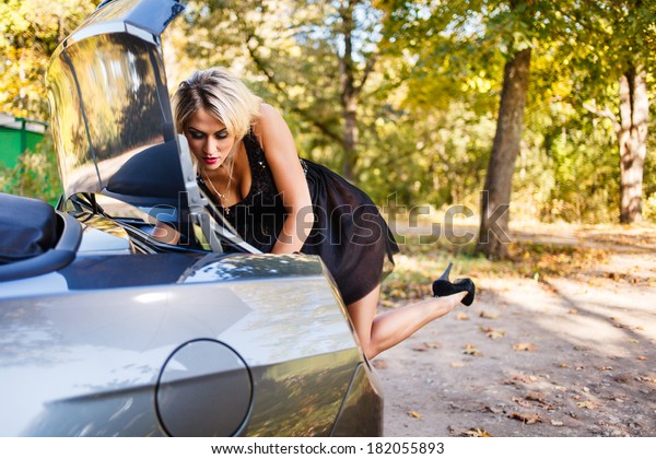 Blond woman\
searching something in  a car\
trunk.