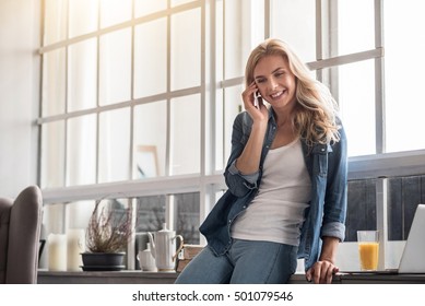 Blond woman talking per mobile phone near window