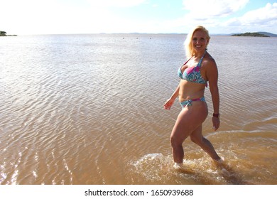 Blond woman walking in the water at the beach wearing a bikini with water and blue sky in the background