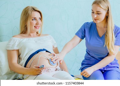 Blond young midwife examination belly of pretty blond pregnant woman with CTG scanning in practice. Pregnancy care. cardiotocography fetal heartbeat examination. Close up