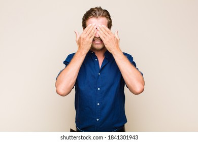 Blonde Adult Caucasic Man Smiling And Feeling Happy, Covering Eyes With Both Hands And Waiting For Unbelievable Surprise