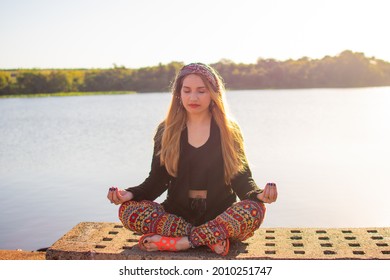A blonde Argentinian woman sitting on a bench with crossed legs and meditating on the riverside