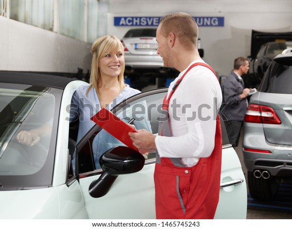 The blonde attractive female customer enter to\
her car and talk to the service men from the car service and looks\
happy and satisfied
