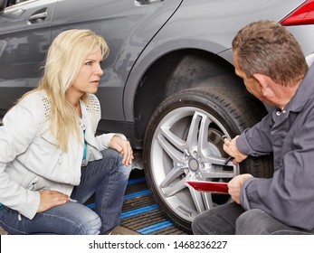 a blonde attractive female customer squads with the car service chef in the workshop in front of her car and he show her something at the tires whats wrong  - Powered by Shutterstock