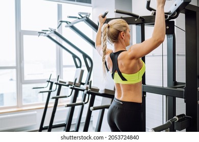 Blonde attractive slim woman wearing sport bra do exercises pull-ups on the horizontal bar in fitness center or gym - Powered by Shutterstock