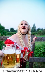 Blonde bavarian female holding a Glass of Beer wearing a Dirndl in garden