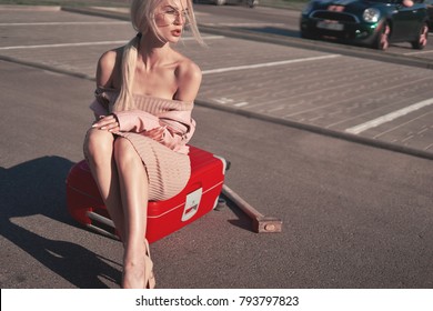Blonde beautiful girl prepare for a trip wait for friends and miss a little on her red bag in pink clothes 