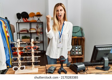 Blonde beautiful young woman working as manager at retail boutique angry and mad raising fist frustrated and furious while shouting with anger. rage and aggressive concept. 