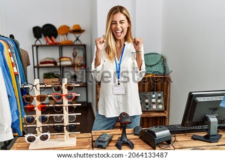 Blonde beautiful young woman working as manager at retail boutique excited for success with arms raised and eyes closed celebrating victory smiling. winner concept. 
