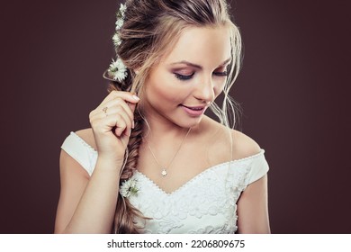 blonde bride with herringbone braid has finger in hair and look down with a little smile on her  face and a luxury engagement ring on her finger