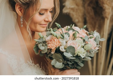 A blonde bride in a veil, in a white dress, holds a bouquet in her hands, beige background