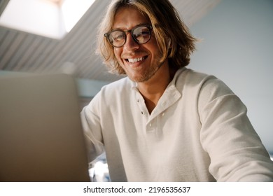 Blonde Bristle Man In Earphones Laughing While Working With Laptop At Home