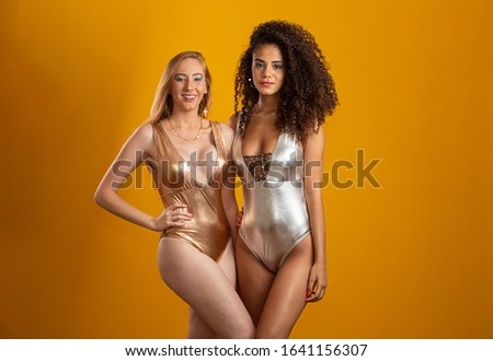 Blonde and brunette women having fun portrait against yellow background. A blonde and a brunette. Different types of hair. Racial diversity. Friends.