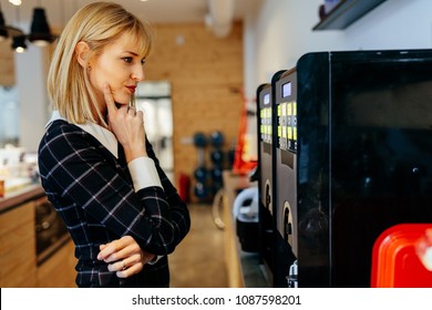 Blonde Businesswoman Standing In Front Of A Coffee Maker In An Office Cafeteria